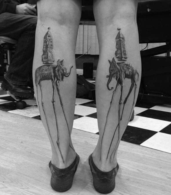 Matching black and grey Salvador Dali-style tattoos on both calves, featuring surreal elephants with elongated legs and obelisks on their backs.