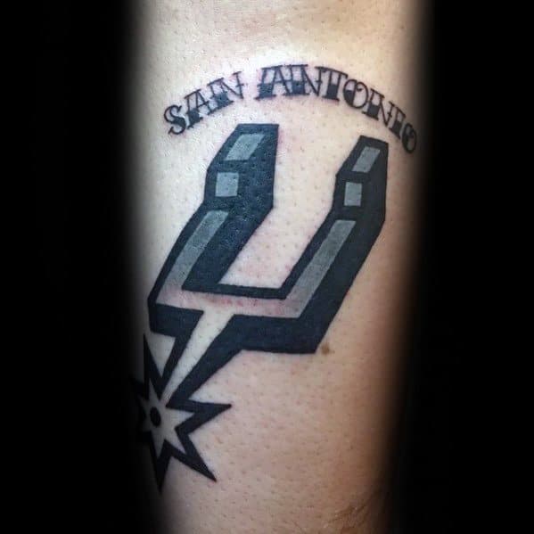 San Antonio Spurs logo tattoo with bold black and grey shading, paired with “San Antonio” text arched above in stylized uppercase lettering.