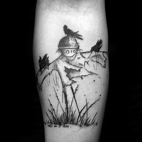 Minimalist scarecrow tattoo with button eyes, tattered clothes, perched crows, and simple grass details in black linework style.