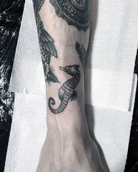 Small seahorse tattoo on wrist, featuring fine linework and minimal shading for a delicate and understated design.