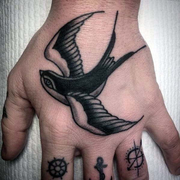 A hand tattoo of a black and white swallow flying on the back of the hand