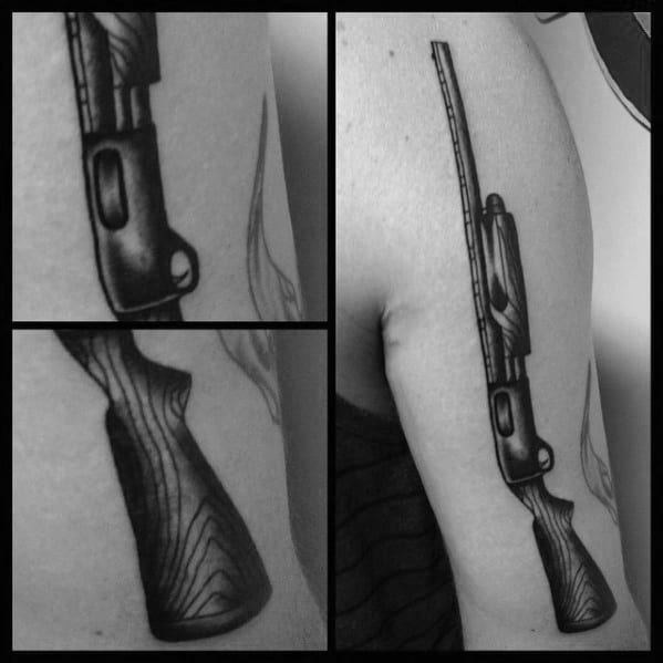 Black and grey shotgun tattoo on the upper arm, featuring detailed wood grain texture and bold shading for a realistic firearm design.