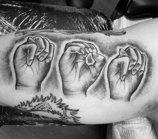 realistic black and grey tattoo of hands signing a word in American Sign Language, detailed with shading and placed along the upper arm
