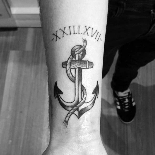 Black and gray anchor tattoo with a wrapped rope and Roman numerals above, symbolizing strength, stability, and a significant personal date.