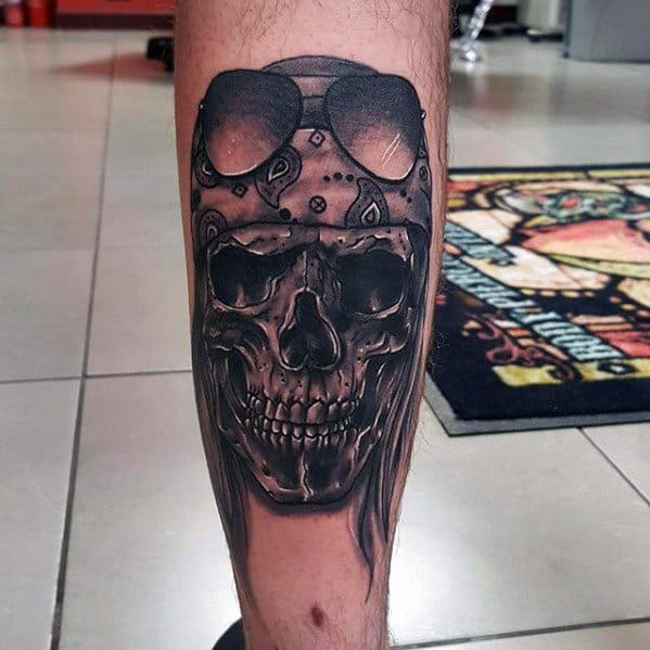 Dark and detailed leg tattoo of a skull wearing a patterned bandana and sunglasses, inspired by the iconic look of Guns N' Roses.