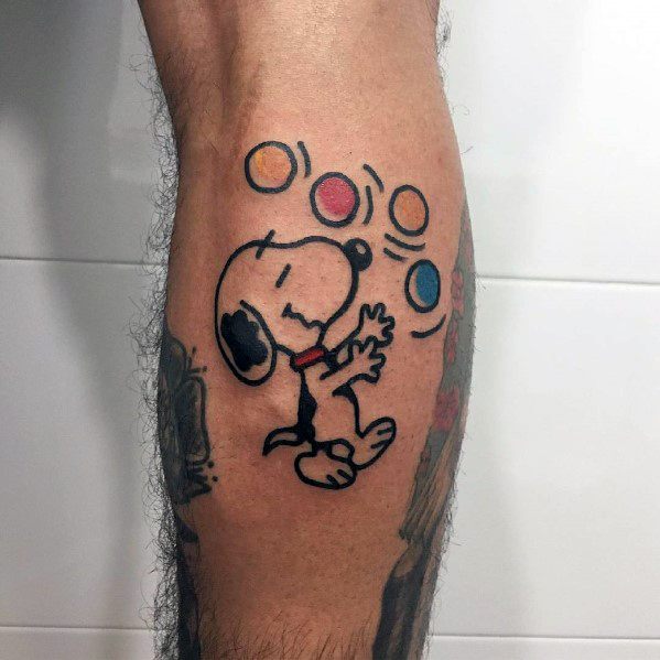 Colorful tattoo of Snoopy joyfully dancing with a red collar, surrounded by floating circles in yellow, red, and blue, placed on a leg.