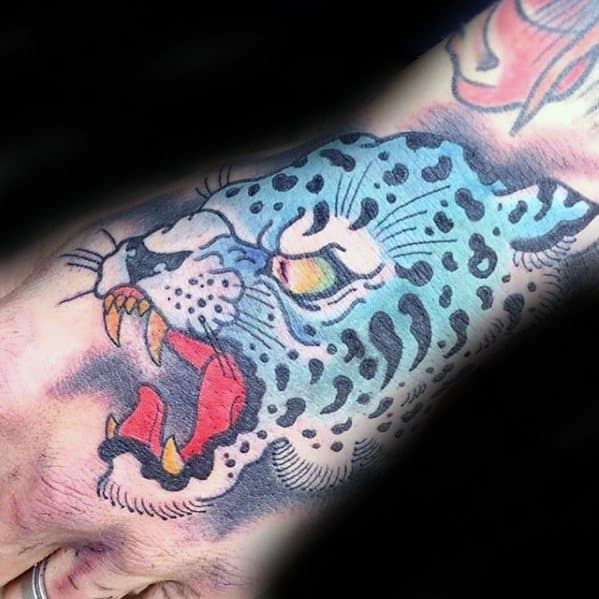 Vibrant snow leopard tattoo on the hand, featuring bold blue tones, fierce expression, and traditional-style outlines with red accents.