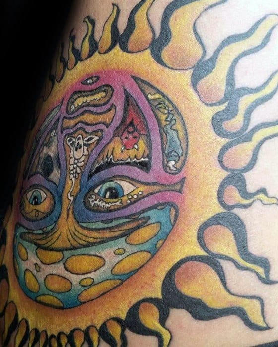 Close-up of a colorful Sublime sun face tattoo with surreal, detailed elements and bold yellow and black flame rays.