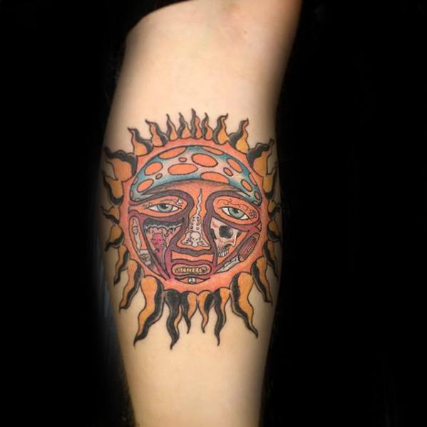 Colorful Sublime sun face tattoo with expressive features and bold black flame rays, placed on the inner forearm.