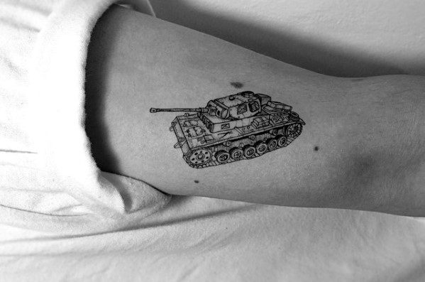 Small, fine-line tank tattoo on the upper arm with intricate detailing and a clean, minimalist black ink design.