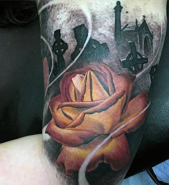A tattoo of a rose with Gothic crosses, a church, and a haunting graveyard on an arm