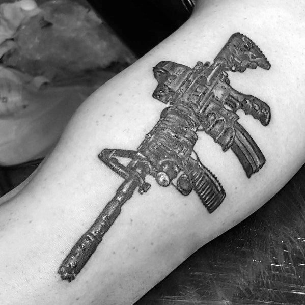 Black and grey AR-15 tattoo on the forearm, featuring intricate details, a tactical grip, and a scope, symbolizing strength, precision, and readiness.