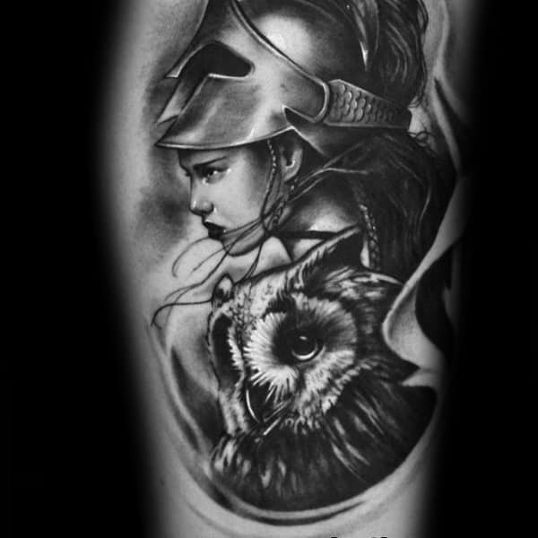 Realistic Athena tattoo with a side-profile face in helmet and a detailed owl below, in soft black and grey shading on upper arm