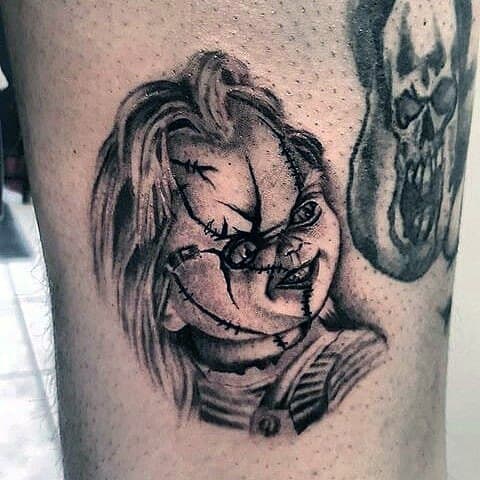 Black and grey Chucky tattoo with bold shading, featuring his stitched face, sinister grin, and intense gaze for a classic horror-inspired design.
