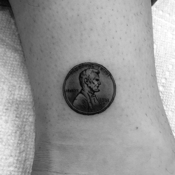 Realistic tattoo of a 1993 Lincoln penny on the ankle, featuring fine details and shading for a miniature coin effect.