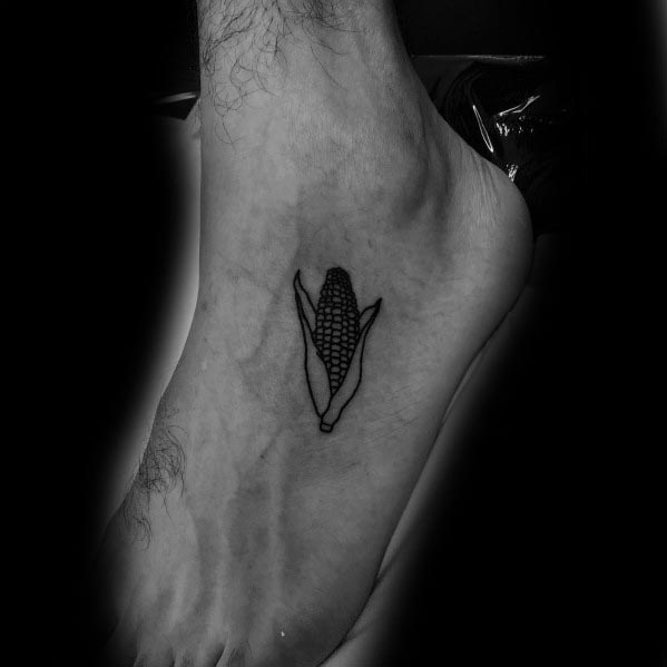 Minimalist black ink tattoo of a small corn cob with husks, placed on the foot for a simple yet bold design.