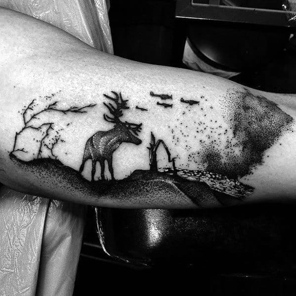 Minimalist black and grey elk tattoo on the arm, featuring dotwork shading, a scenic landscape, and flying birds for a serene, artistic design.