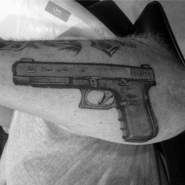Realistic black and grey tattoo of a Glock pistol on the forearm, featuring fine details and shading for a bold and three-dimensional effect.