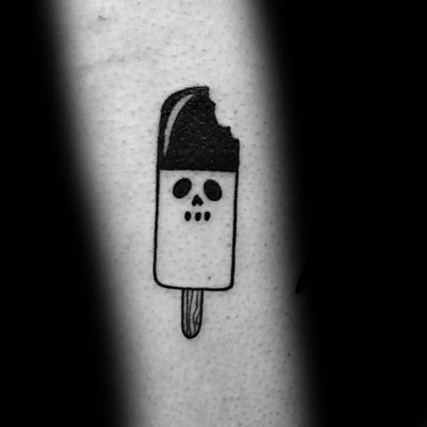 Minimalist black ink tattoo of a bitten chocolate-dipped popsicle with a simple skull face design, blending cute and spooky aesthetics.