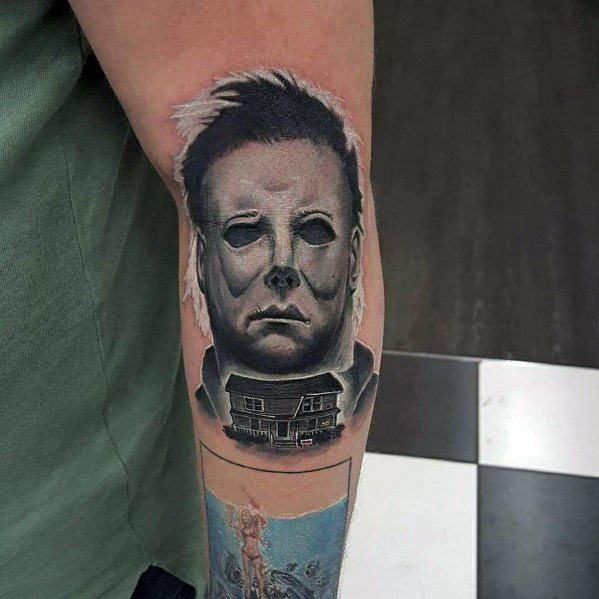 Realistic Michael Myers tattoo on the forearm, featuring his eerie mask with the iconic Myers house below for a chilling horror look.