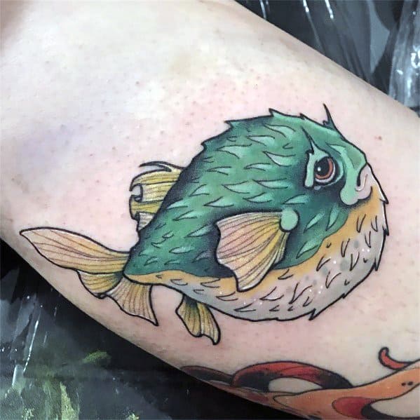 Vibrant pufferfish tattoo with green and yellow hues, fine shading, and bold outlines, giving it a dynamic and lifelike appearance.