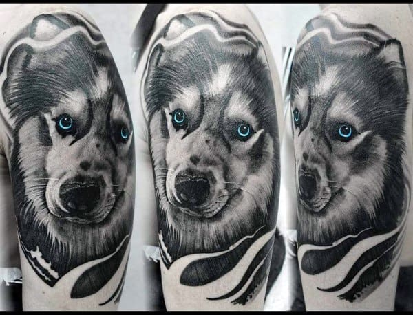 Black and gray Siberian Husky tattoo on a man's arm, featuring striking blue eyes and bold shading for a powerful and lifelike design.