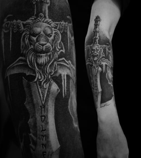 Black and grey tattoo of the Alliance lion sword from World of Warcraft, featuring intricate shading and medieval details, inked on the forearm.