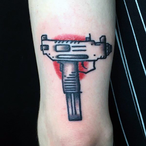 Black Uzi tattoo on the forearm with a red circular background. Bold lines and shading create a striking contrast against the skin.