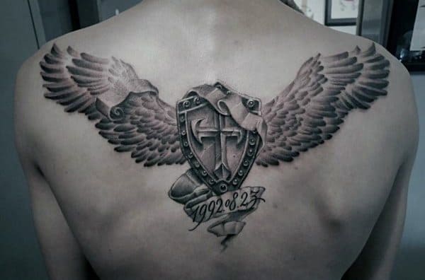 Black and grey upper back tattoo of a winged shield with a cross, featuring a scroll beneath with the date “1992.8.27” in script.