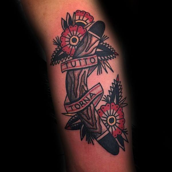 Boomerang tattoo with woodgrain detail, red flowers, and a ribbon wrapping around it reading TUTTO TORNA on the forearm.