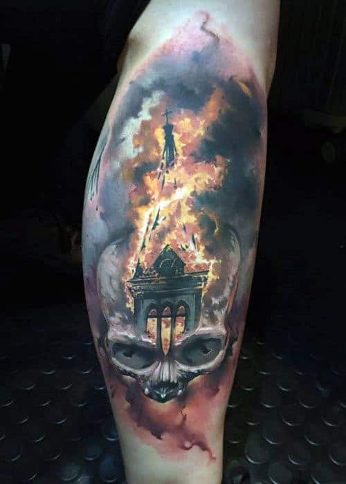 Realistic burning church tattoo with intense orange flames and smoke. The base transforms into a dark, ominous skull on the calf.
