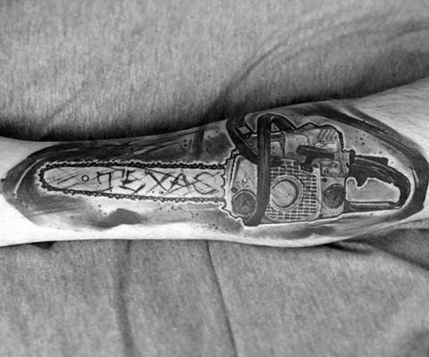 Realistic black and gray forearm tattoo of a chainsaw with the word "TEXAS" carved into the blade, inspired by horror themes.