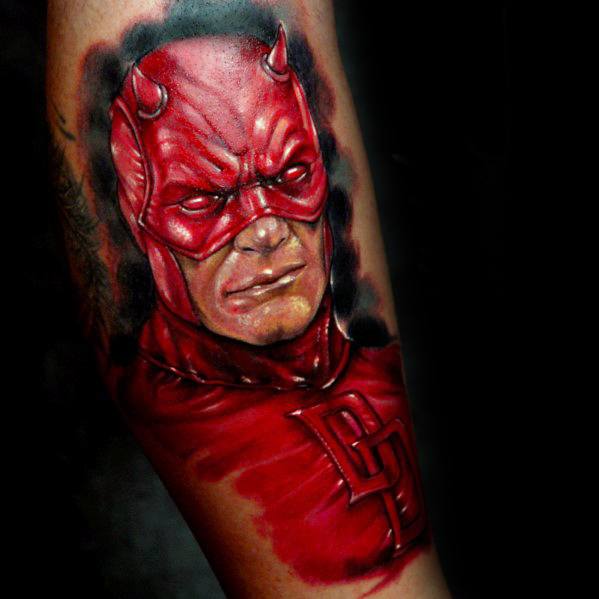 Hyper-realistic Daredevil tattoo with intense red tones, lifelike texture, sharp expression, and bold DD logo on the chest.