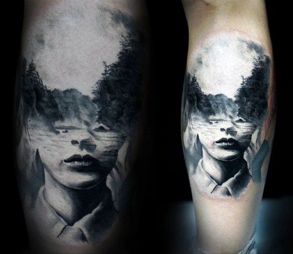 Black and grey double exposure tattoo of a woman's face merging into a misty river and forest scene, blending realism with dreamlike nature.