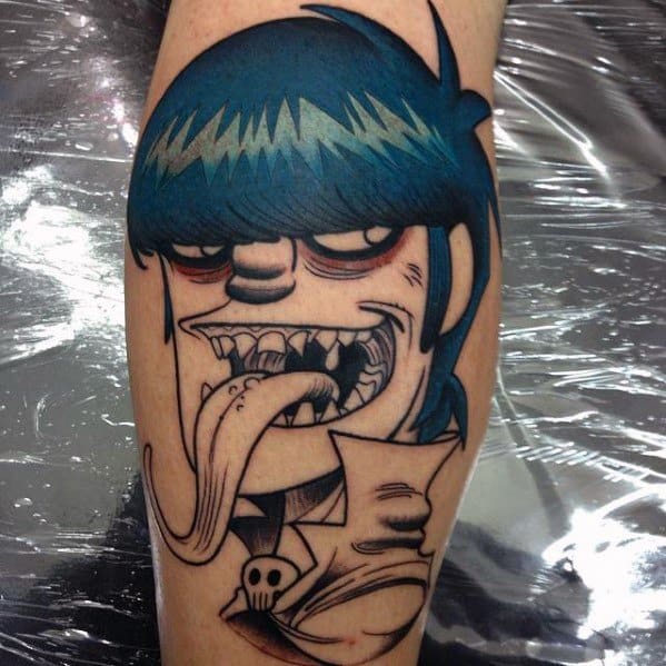 Bold color tattoo of Murdoc from Gorillaz with a wild grin, tongue out, blue hair, and exaggerated features outlined in thick black ink.