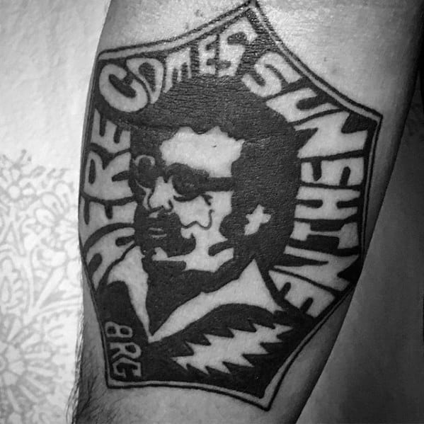 Blackwork Grateful Dead tattoo featuring a stylized portrait with the phrase “Here Comes Sunshine” and bold lightning bolt accents.