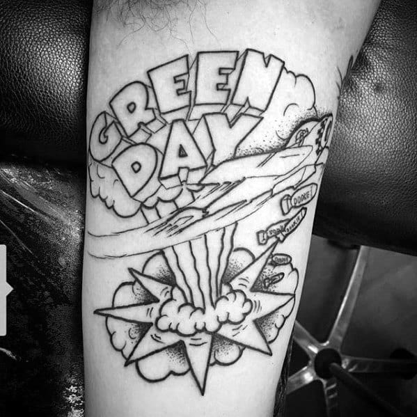 Black and white tattoo of a comic-style plane dropping bombs with “Green Day” in bold letters above and explosion clouds below.