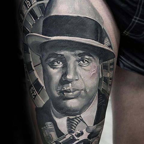 Al Capone tattoo featuring a detailed black-and-white portrait of the gangster with his iconic fedora, surrounded by a roulette wheel and a vintage gun.