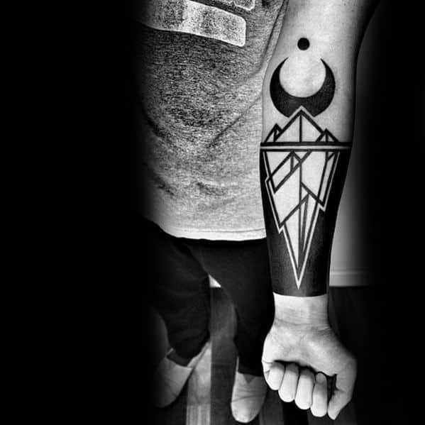 Bold geometric iceberg tattoo on the forearm with sharp blackwork, crescent moon, and dot above, forming a striking symmetrical design.