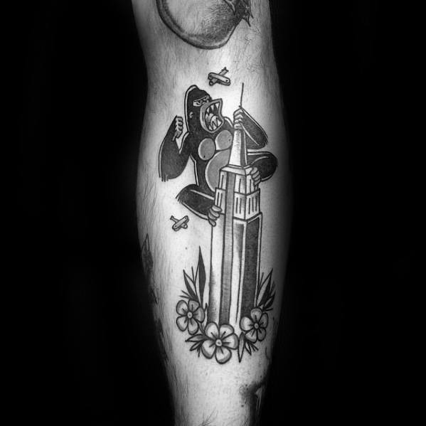 Black and grey traditional-style King Kong tattoo featuring Kong on a skyscraper, surrounded by planes and floral elements at the base.