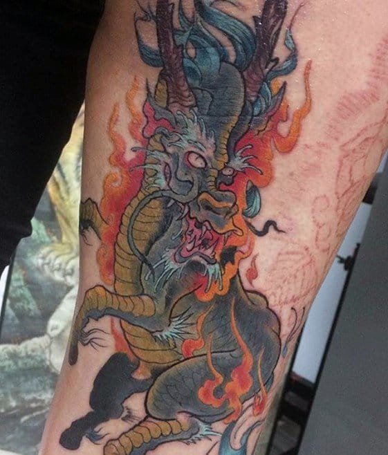 Fierce Kirin tattoo with dark scales, golden belly, and multicolored flames, captured in a roaring pose with glowing white eyes.
