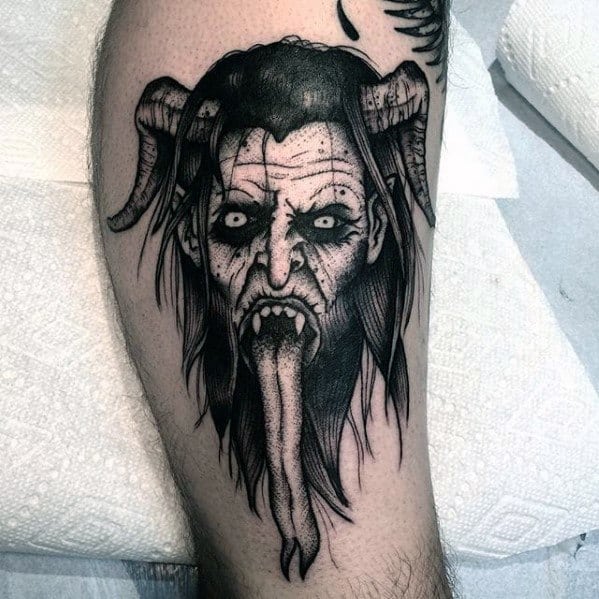 Black and grey Krampus tattoo featuring a haunting horned face with hollow eyes, sharp fangs, and an exaggeratedly long tongue.