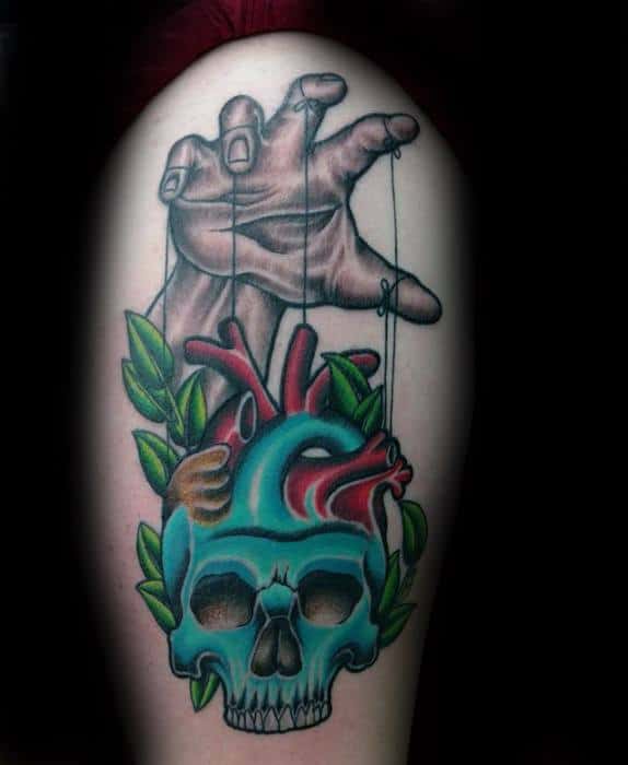 Colorful puppet tattoo of a hand controlling a skull-heart hybrid with leaves, blending life and death themes in a bold, surreal style.