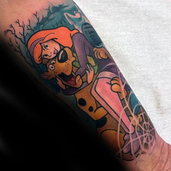 Tattoo of Daphne hugging a scared Scooby-Doo in a spooky forest scene with a full moon and bare trees in the background.