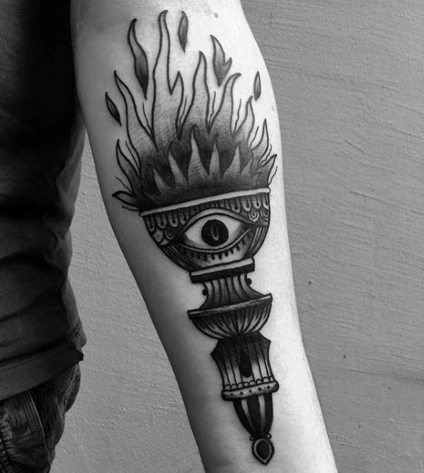 Black and grey torch tattoo with soft shaded flames and a central eye motif, designed with bold lines and ornamental details.
