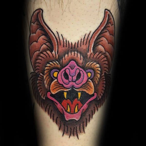 Traditional bat head tattoo in warm tones of brown, pink, and yellow, with bold lines and sharp fangs for a fierce expression.