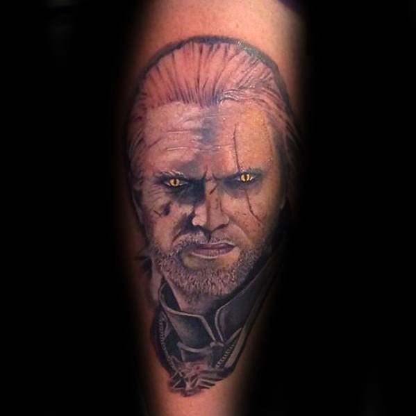 Realistic portrait tattoo of Geralt from The Witcher with piercing yellow eyes and scarred face, featuring his wolf medallion below.