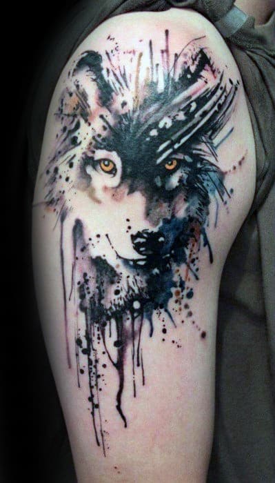 Watercolor wolf tattoo on upper arm with piercing amber eyes, black ink splatters, and dripping effects for a wild, artistic vibe.