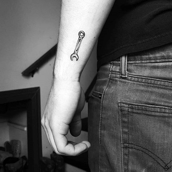 Small black ink tattoo of a simple wrench on the inner wrist, minimalistic in design and placement.