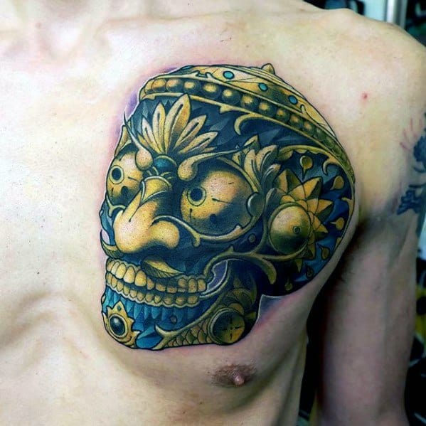 Bold Tibetan skull tattoo on the chest with gold and blue accents, lotus motifs, and intricate ornamental crown detailing.